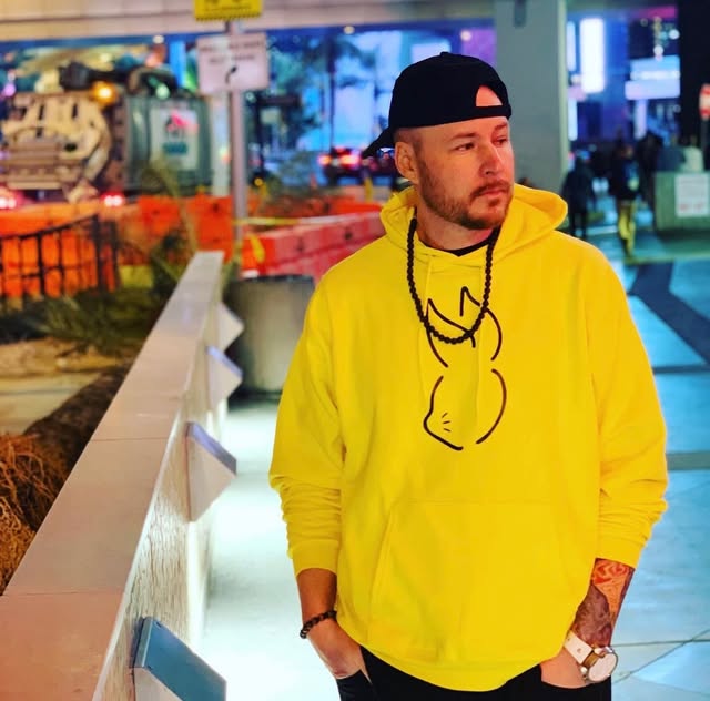 Hypnautic wearing a bright yellow hoodie in an arcade